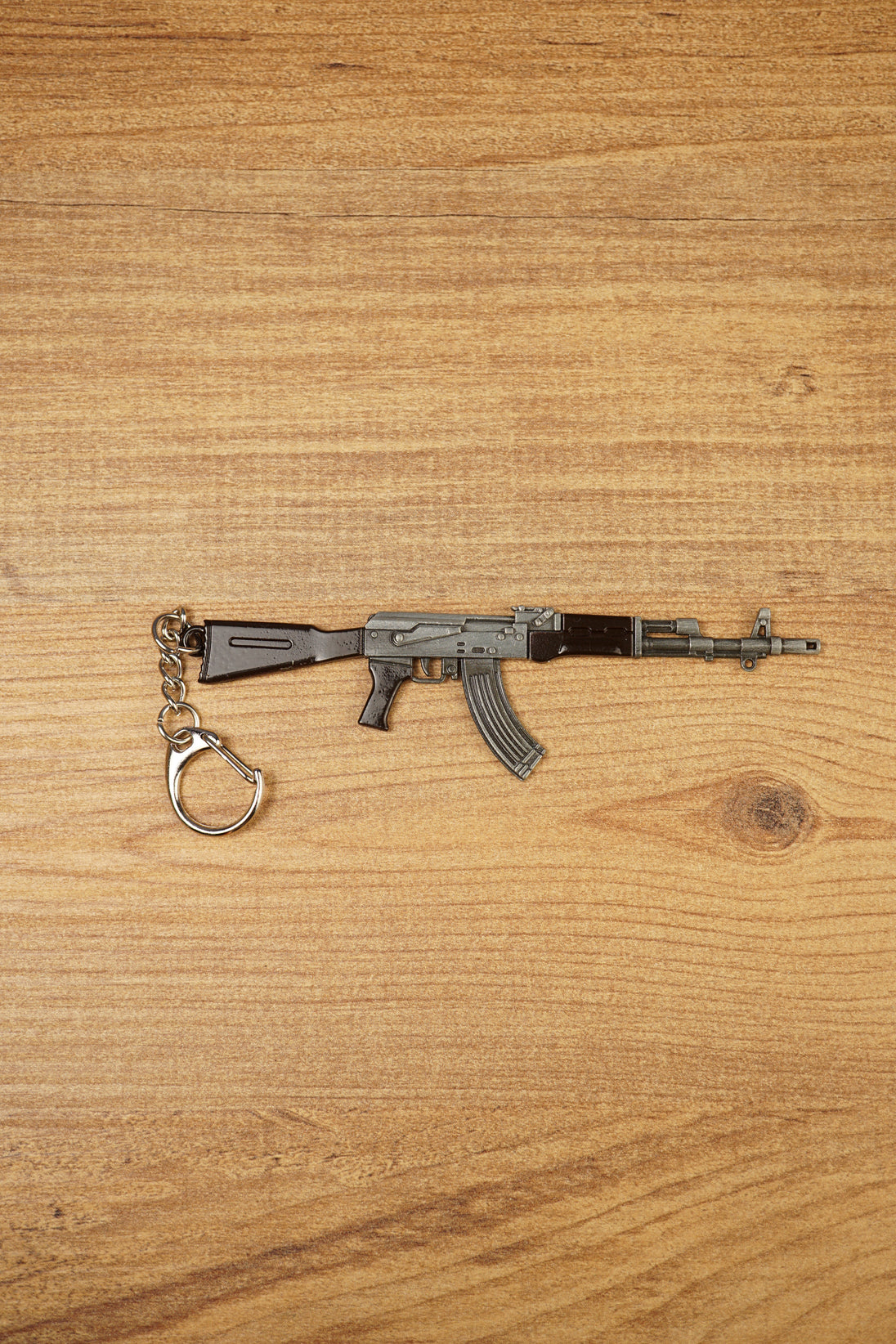 Classic black AKM 7.62x39 rifle keychain replica side view with metal keyring attachment on a wooden tabletop background