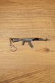 Classic black AKM 7.62x39 rifle keychain replica side view with metal keyring attachment on a wooden tabletop background