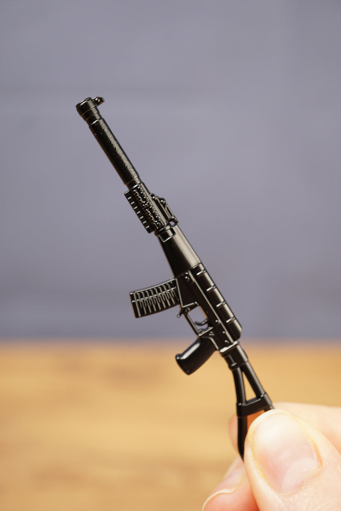 Black tactical rifle keychain held upright, showing long suppressor, curved magazine and folding stock style silhouette