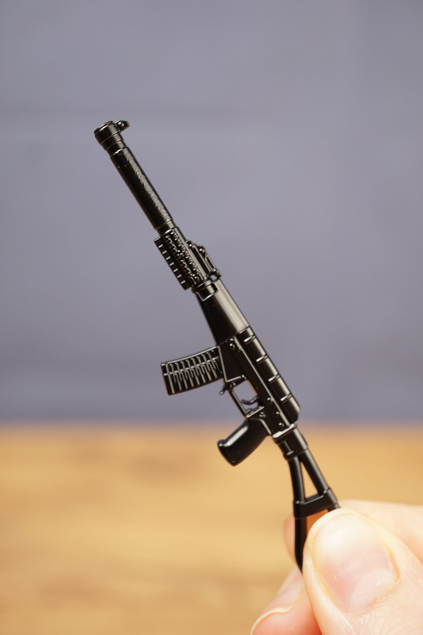 Black tactical rifle keychain held upright, showing long suppressor, curved magazine and folding stock style silhouette
