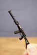 Black tactical rifle keychain held upright, showing long suppressor, curved magazine and folding stock style silhouette