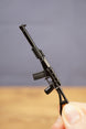Black tactical rifle keychain held upright, showing long suppressor, curved magazine and folding stock style silhouette