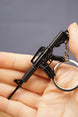 Black tactical rifle keychain close-up with metal key loop, designed as a compact FPS gamer backpack charm.