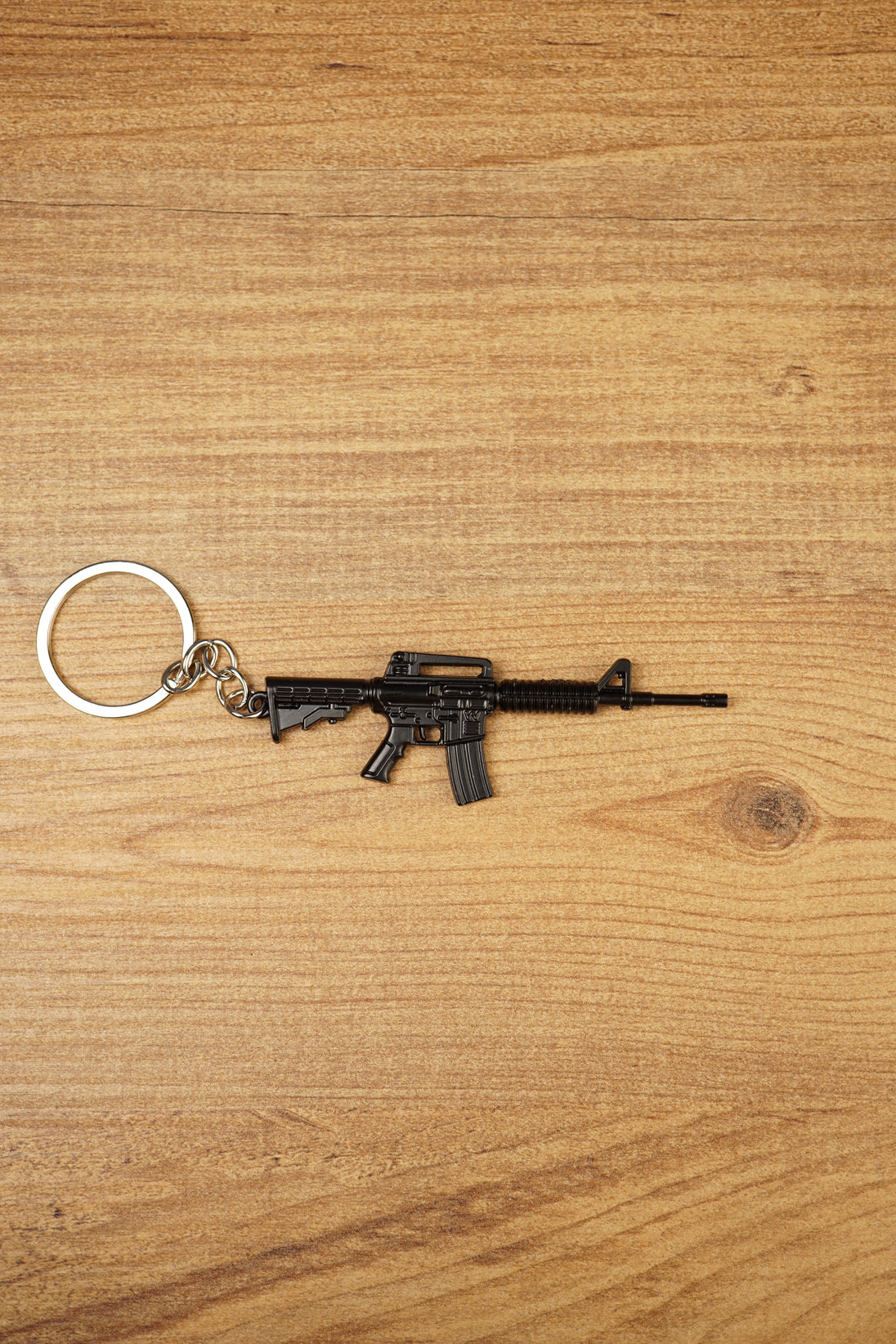Black tactical rifle keyring with metal chain and key loop on a wooden surface, ideal as an FPS gamer gift.
