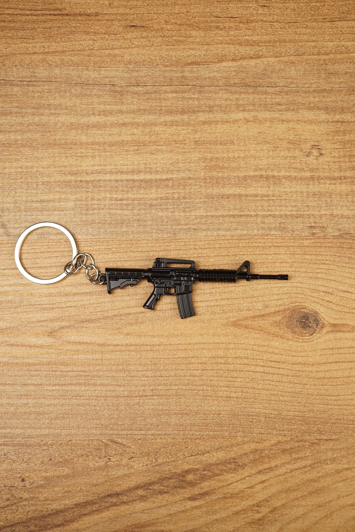 Black tactical rifle keyring with metal chain and key loop on a wooden surface, ideal as an FPS gamer gift.