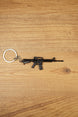 Black tactical rifle keyring with metal chain and key loop on a wooden surface, ideal as an FPS gamer gift.