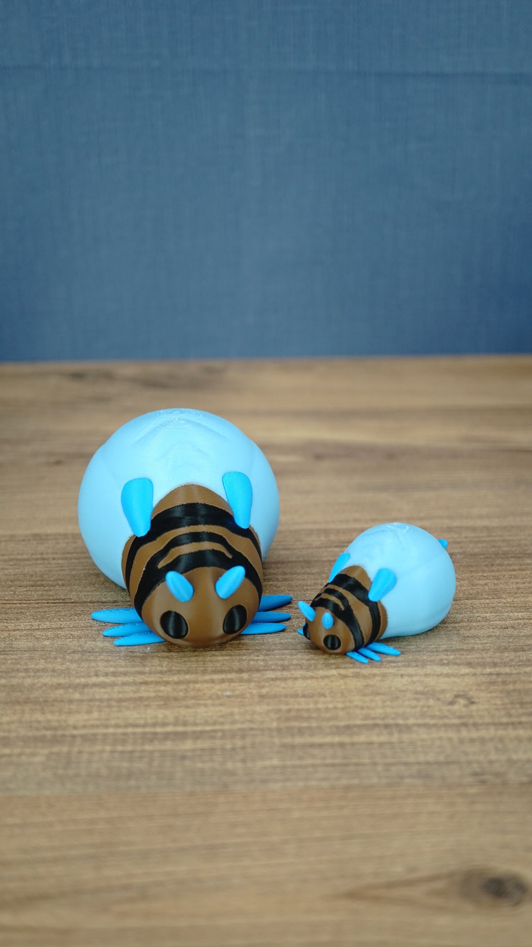 Large and small blue Palia-inspired lantern bug plush figures displayed together on a wooden tabletop.