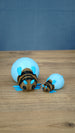 Large and small blue Palia-inspired lantern bug plush figures displayed together on a wooden tabletop.