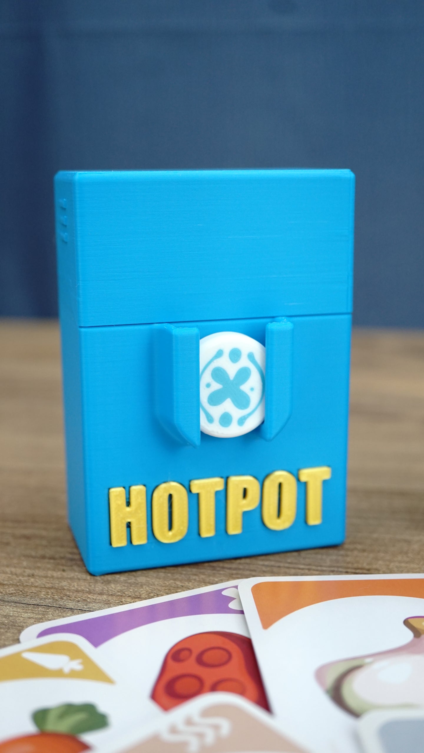 Blue 3D printed Palia Hotpot storage case with gold Hotpot lettering, displayed with ingredient cards in front.