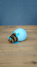 Blue Palia-inspired lantern bug plush figure shown from the front on a wooden tabletop.