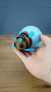 Hand holding a blue Palia-inspired lantern bug plush figure to show its size and details.