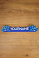 Top-down view of a blue Palia-inspired custom nameplate on a wood surface, with white lettering, light blue swirls, and star decorations