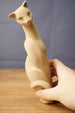 Close-up of a beige 3D printed cat figurine replica held by hand, highlighting the long neck, stylized face, curved body, and print texture.