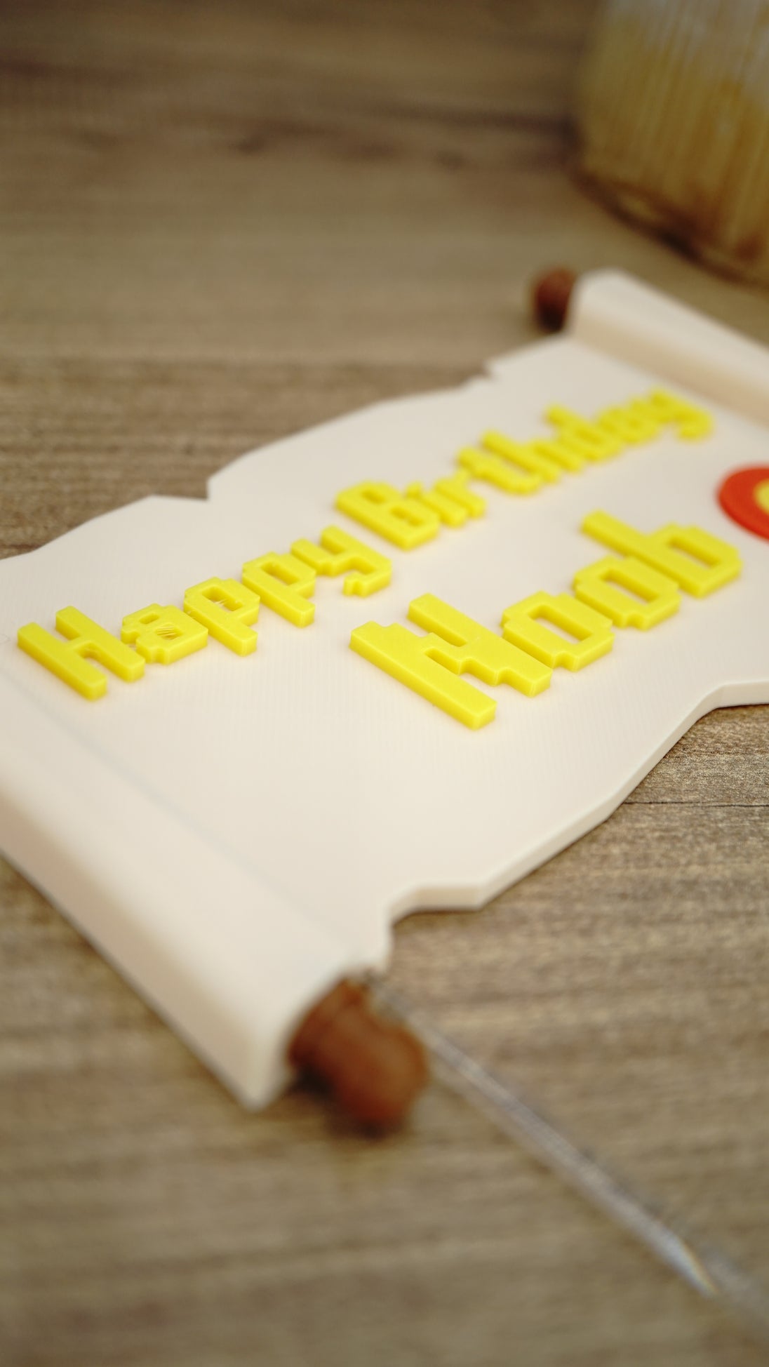 Detailed close-up of yellow raised Happy Birthday Noob lettering on a fantasy quest scroll cake topper for gamer birthday parties.