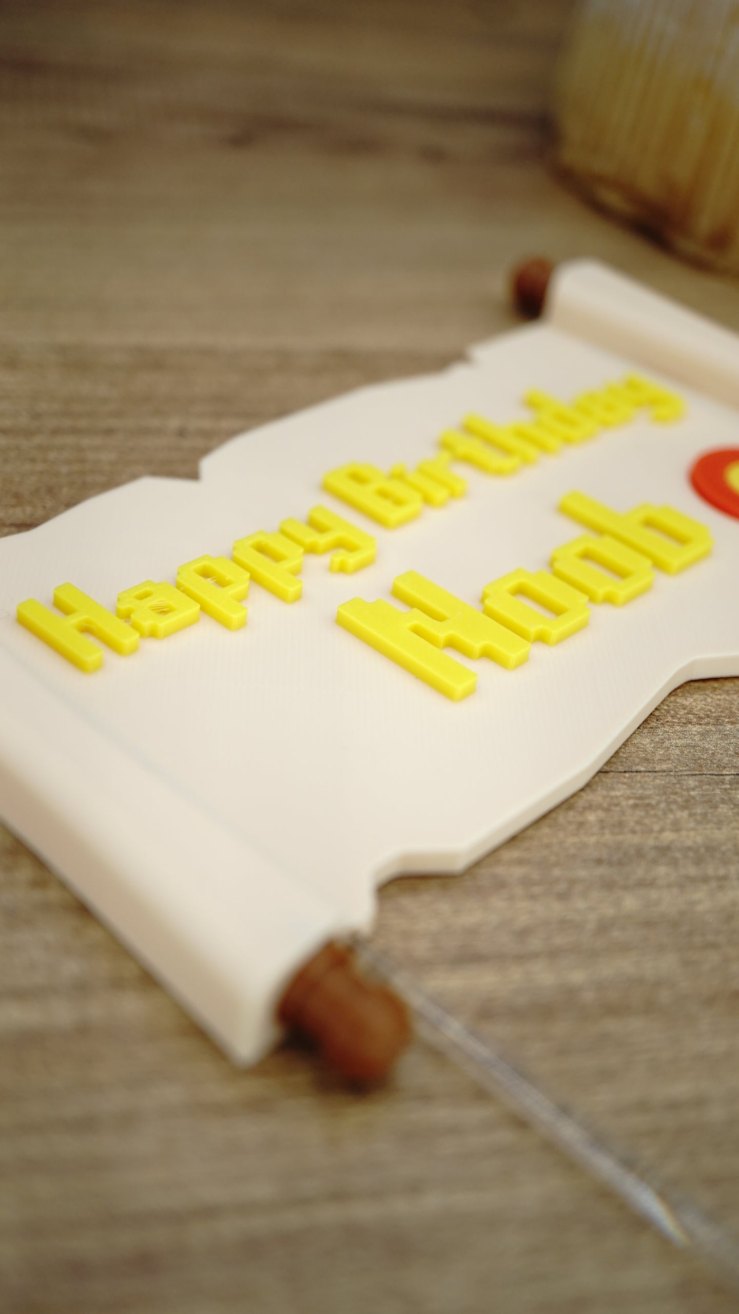 Detailed close-up of yellow raised Happy Birthday Noob lettering on a fantasy quest scroll cake topper for gamer birthday parties.