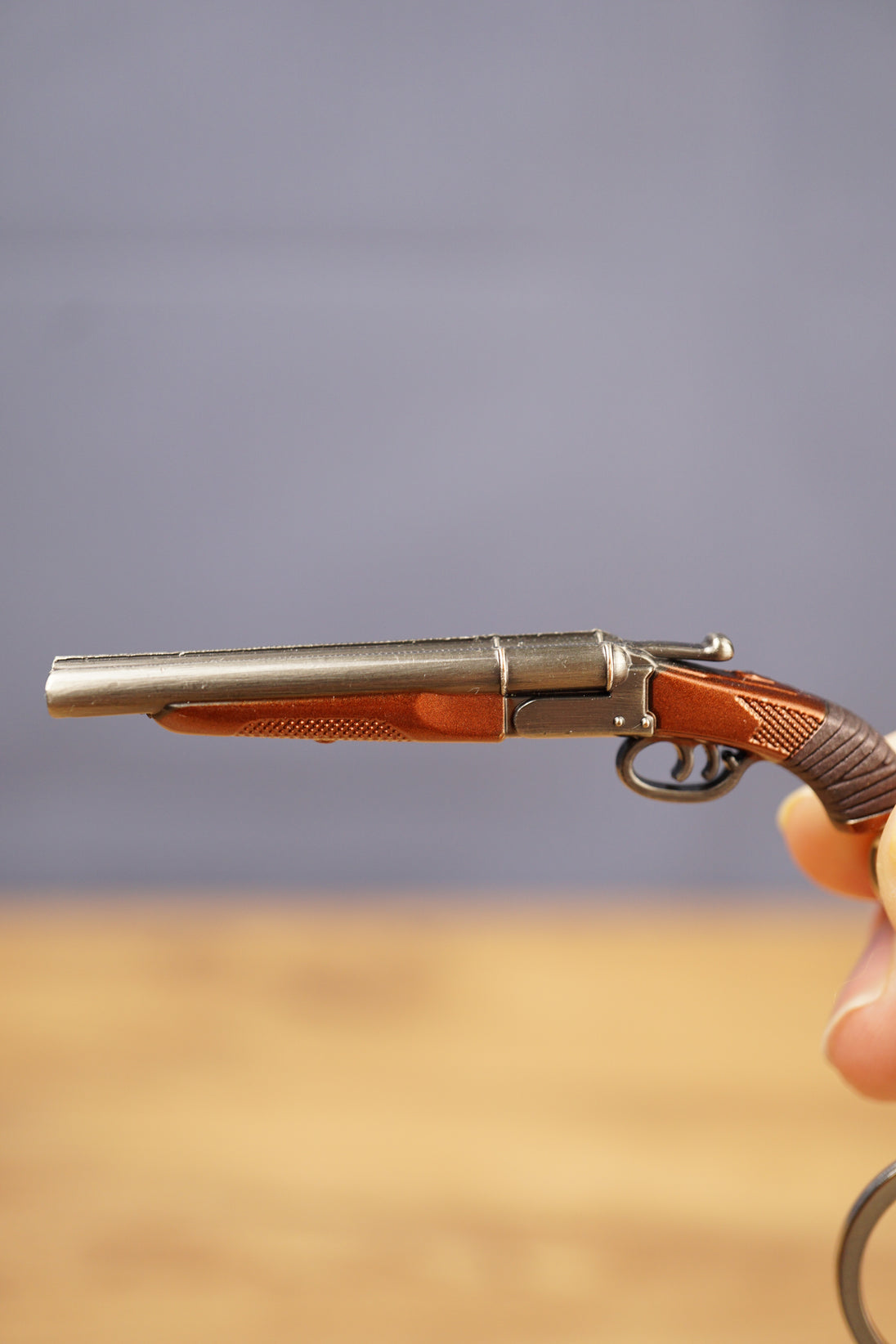 Close-up of miniature double-barrel shotgun keychain showing gunmetal finish, brown grip detail and realistic tactical collectible styling