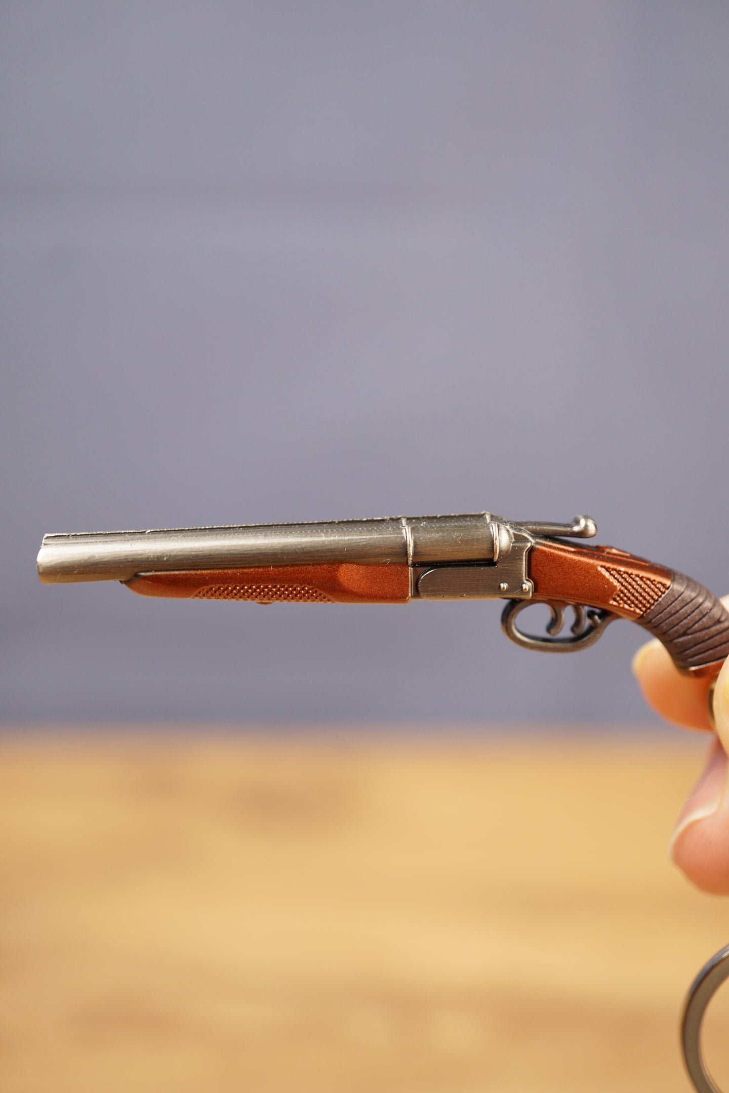 Close-up of miniature double-barrel shotgun keychain showing gunmetal finish, brown grip detail and realistic tactical collectible styling