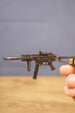 Close-up of a metal UMP45-style submachine gun keyring held between fingers, showing compact scale and detailed tactical design