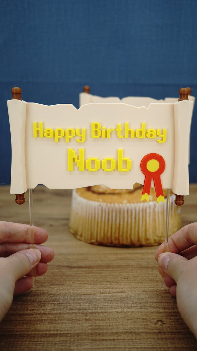 Hands holding a custom Happy Birthday Noob quest scroll cake topper with clear acrylic sticks, ready to place into a gamer birthday cake.