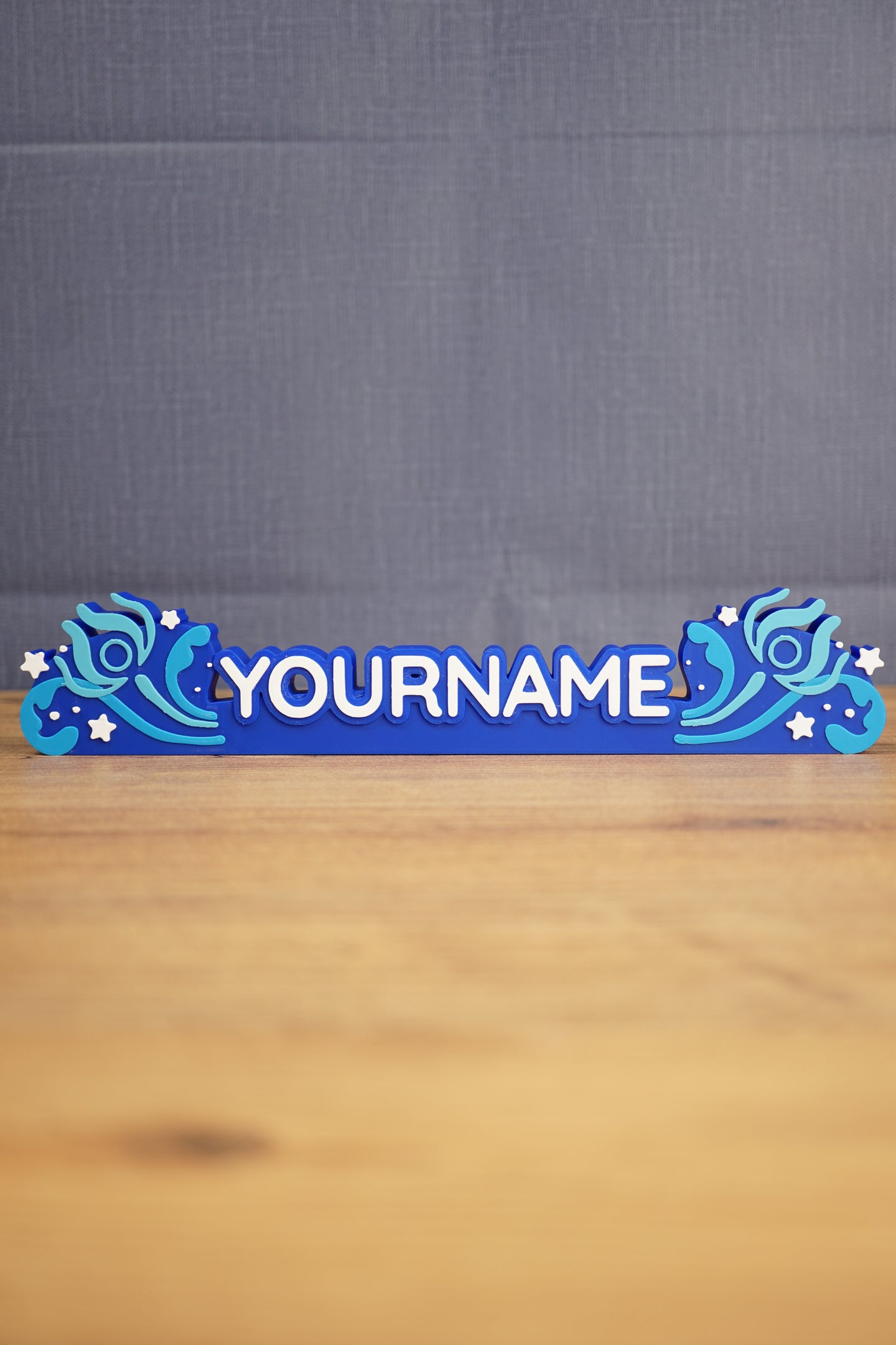 Custom blue Palia-inspired One-in-Ten-Million nameplate with white raised lettering, stars, and decorative swirl details on a wooden desk