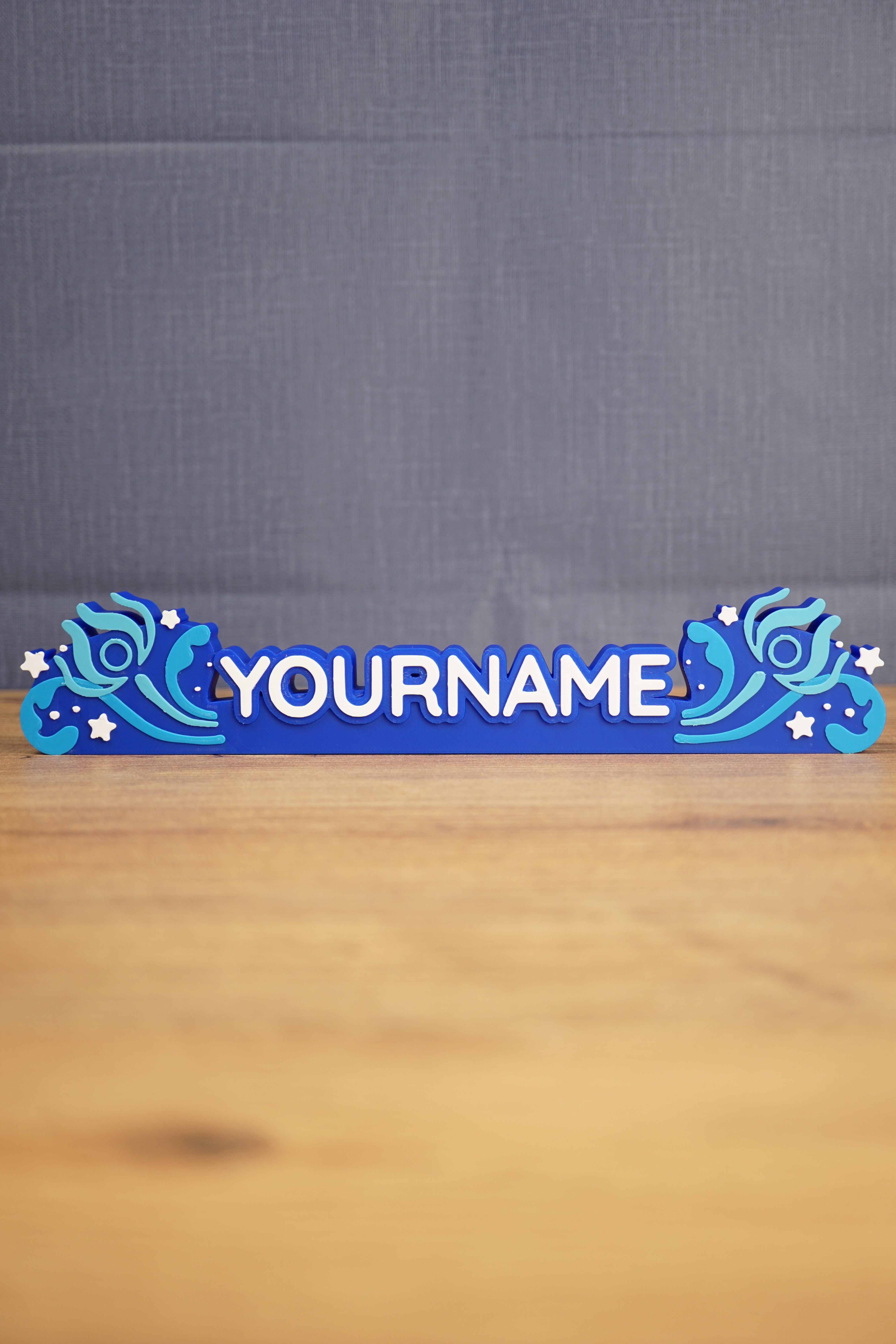 Custom blue Palia-inspired One-in-Ten-Million nameplate with white raised lettering, stars, and decorative swirl details on a wooden desk