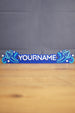 Custom blue Palia-inspired One-in-Ten-Million nameplate with white raised lettering, stars, and decorative swirl details on a wooden desk