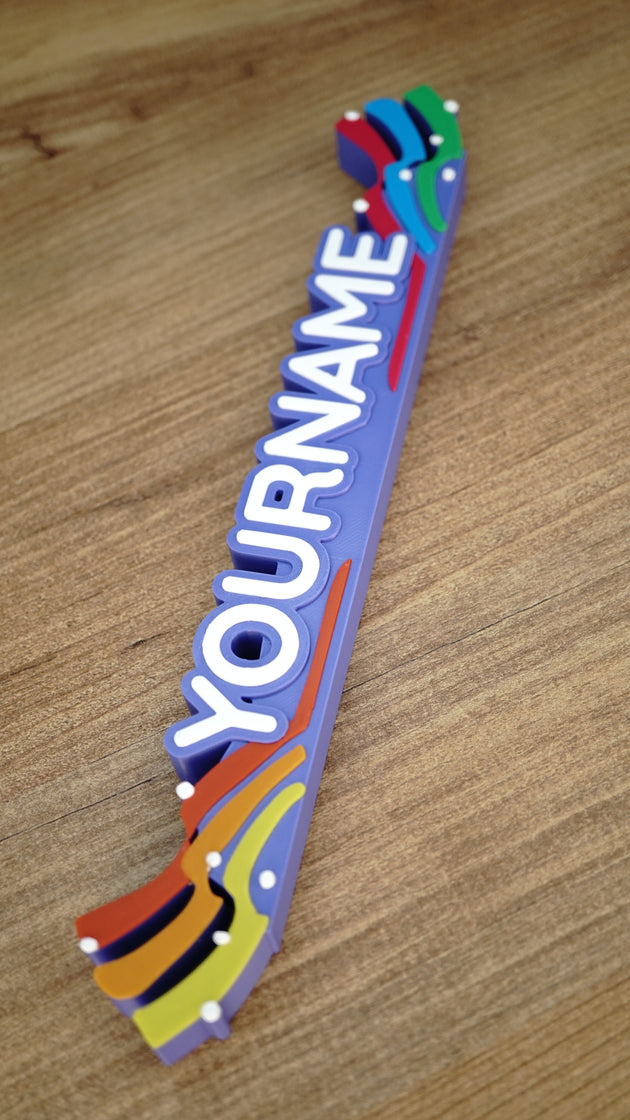Angled top view of a custom Palia Prismatic Pride nameplate showing raised white letters, layered rainbow details, and a purple display base.