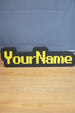 Custom YourName LED sign with RuneScape-style font, black casing, and bright yellow lettering on a wooden tabletop.