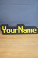 Custom YourName LED sign with RuneScape-style font, black casing, and bright yellow lettering on a wooden tabletop.