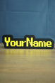 Personalized YourName LED desk sign with RuneScape-style yellow lettering, black casing, and subtle tabletop glow.