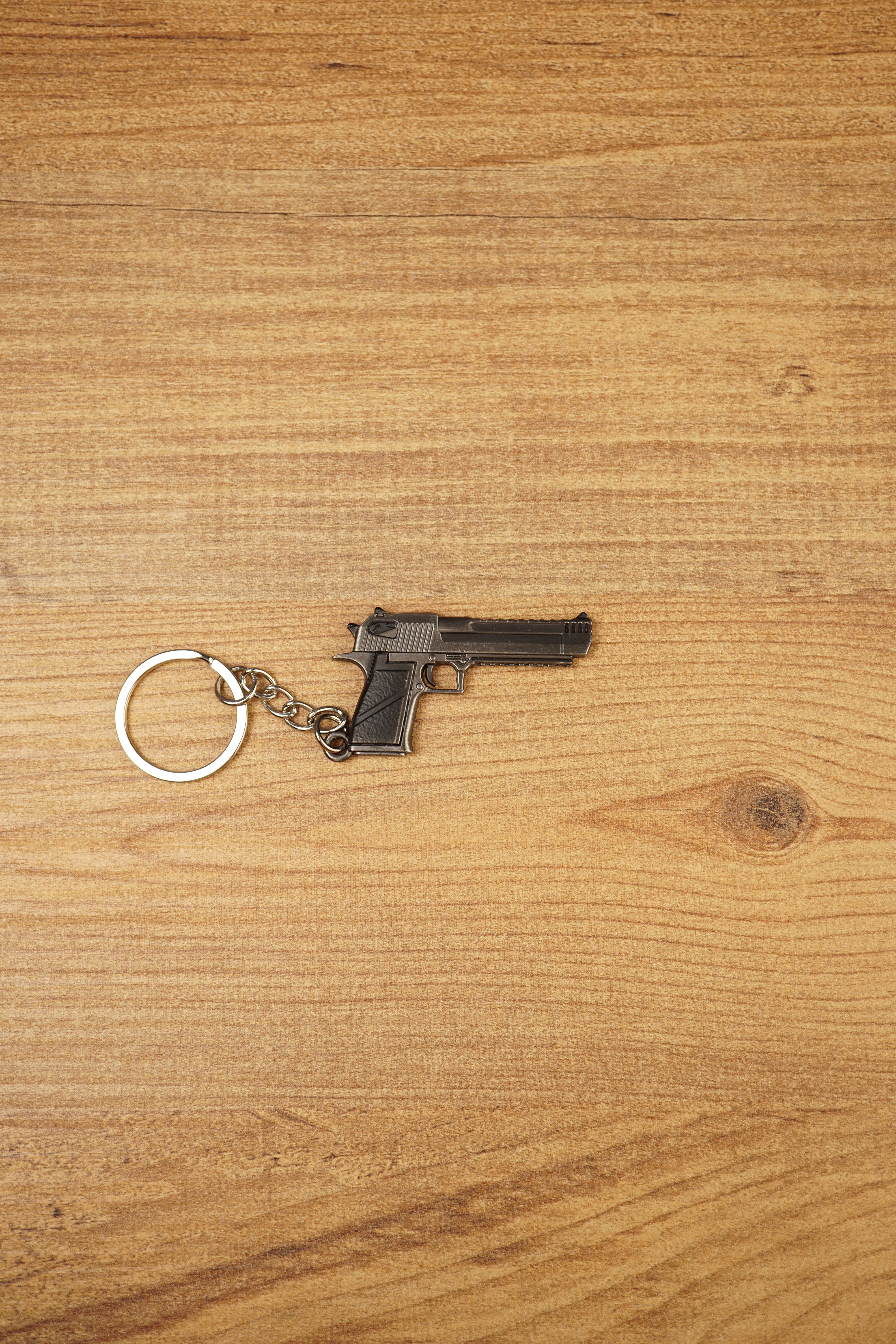 Mini Desert Eagle pistol keychain replica laid flat on a wooden surface, showing the gunmetal finish, black grip and silver split ring attachment
