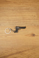 Mini Desert Eagle pistol keychain replica laid flat on a wooden surface, showing the gunmetal finish, black grip and silver split ring attachment