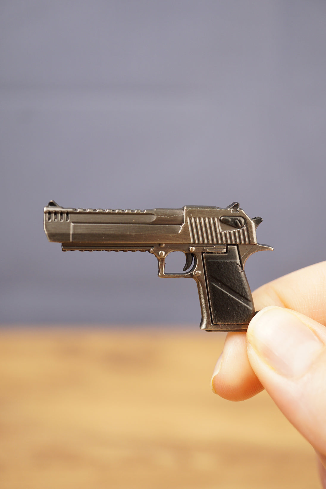 Close-up of a small Desert Eagle-style pistol keychain held between fingers, showing the metallic finish, black handle and detailed side profile