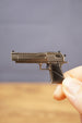 Close-up of a small Desert Eagle-style pistol keychain held between fingers, showing the metallic finish, black handle and detailed side profile