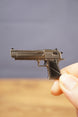 Close-up of a small Desert Eagle-style pistol keychain held between fingers, showing the metallic finish, black handle and detailed side profile