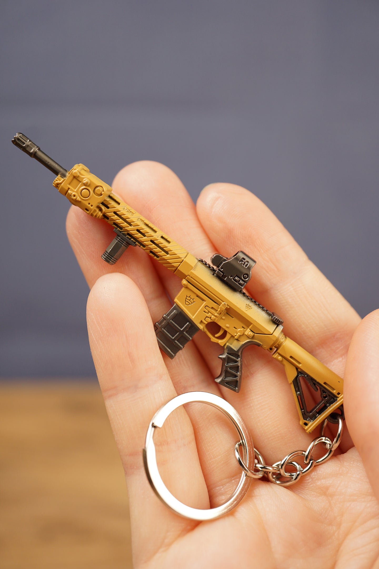Detailed close-up of tan rifle keychain showing metallic finish, sight, magazine and tactical shooter inspired design.