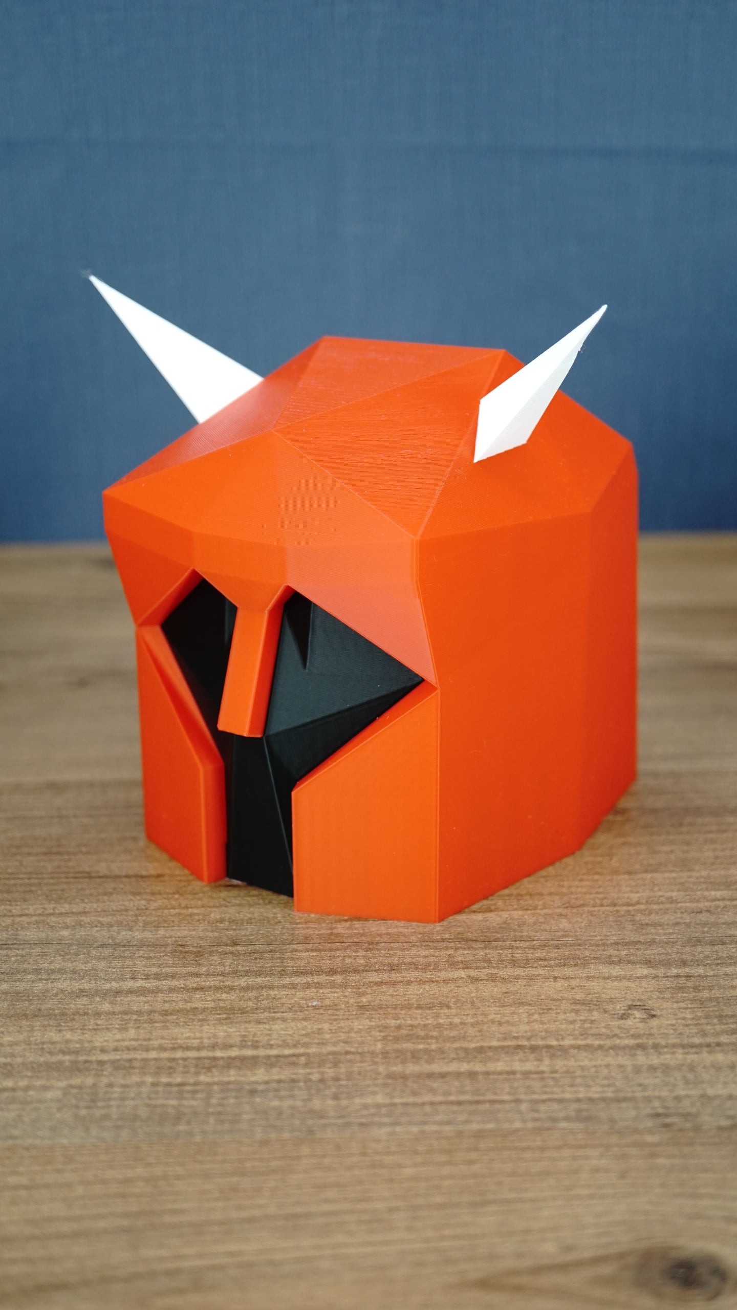 Angled side view of the Dragon Med Helm replica showing the red armour shape, black visor area and white horn details