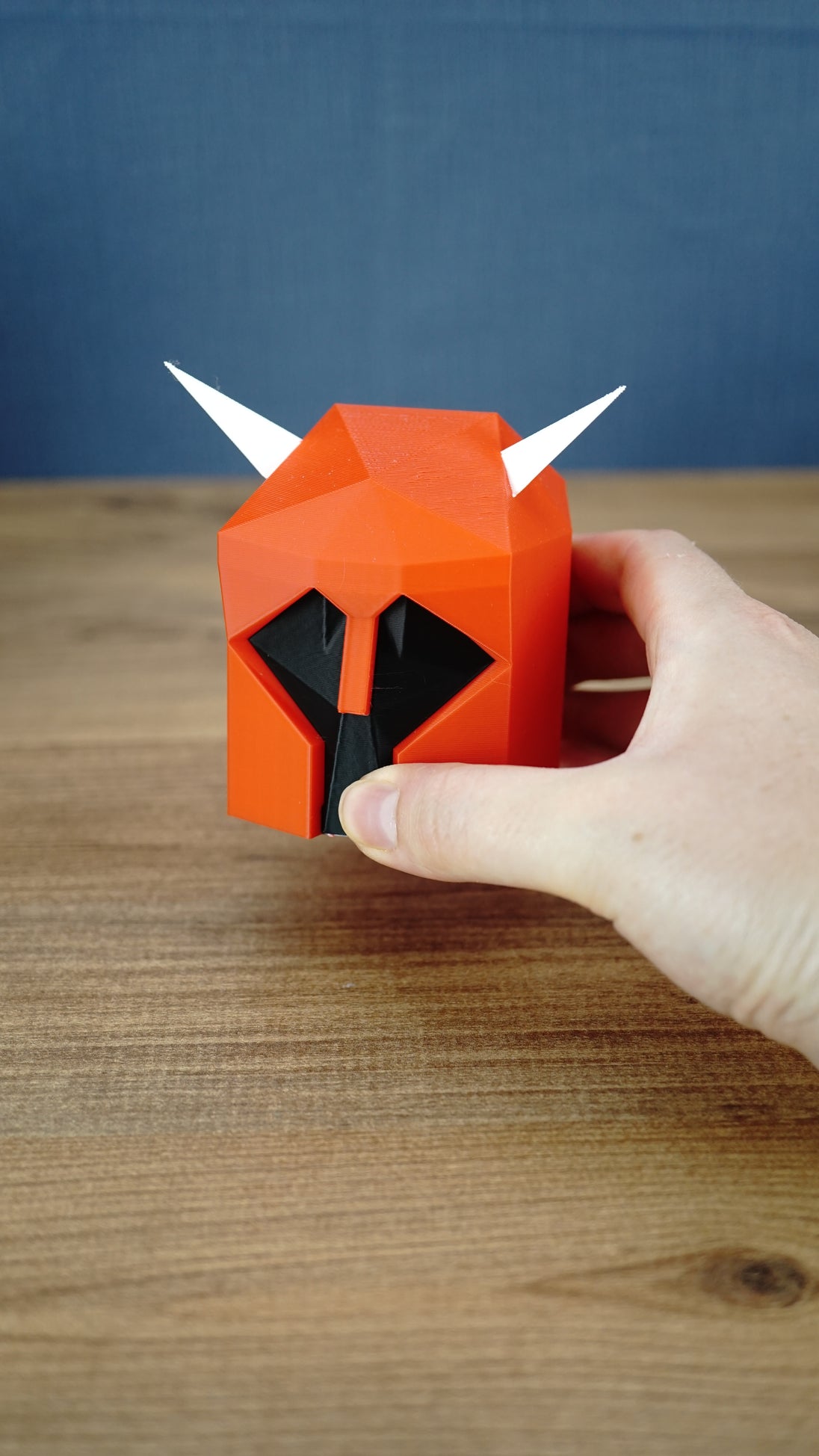 Hand holding the small Dragon Med Helm display replica, showing its compact size, red helmet body, black face and white horns
