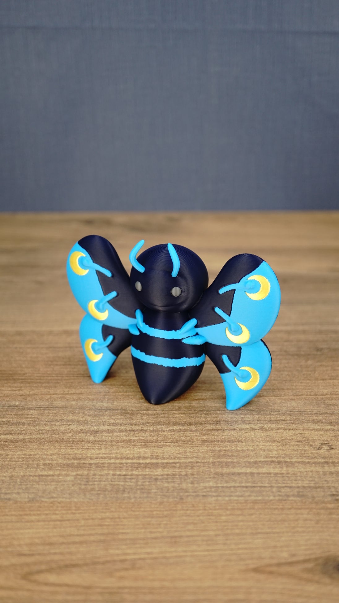 Angled front view of a Duskwing Butterfly plush-inspired collectible showing its rounded body, blue stripes and gold wing markings.