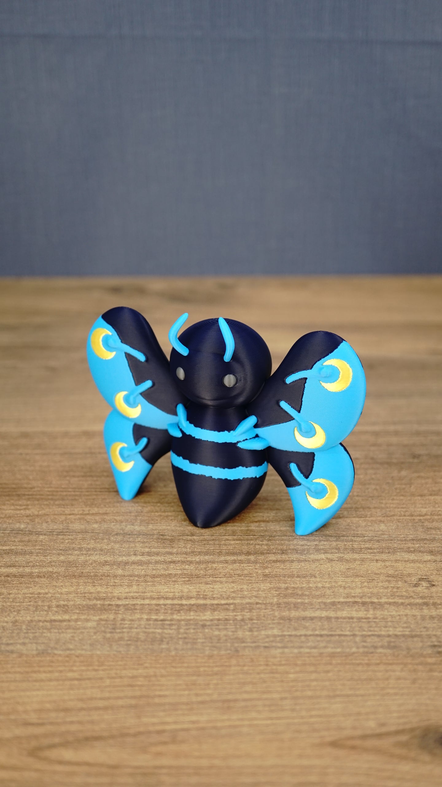 Angled front view of a Duskwing Butterfly plush-inspired collectible showing its rounded body, blue stripes and gold wing markings.