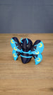 Angled front view of a Duskwing Butterfly plush-inspired collectible showing its rounded body, blue stripes and gold wing markings.