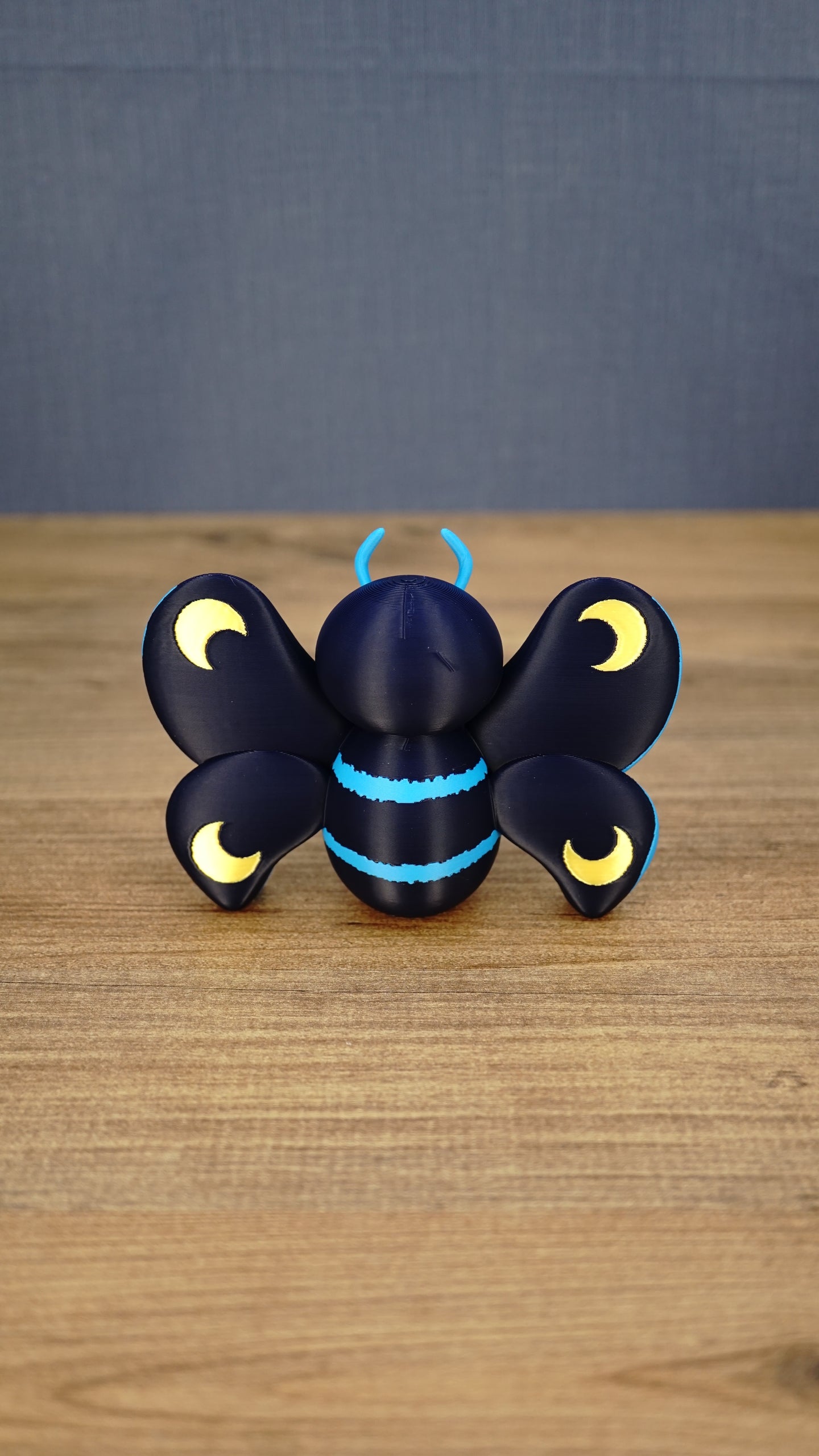 Rear view of the Duskwing Butterfly figure displaying dark-blue wings, four gold crescent markings and bright-blue body stripes.