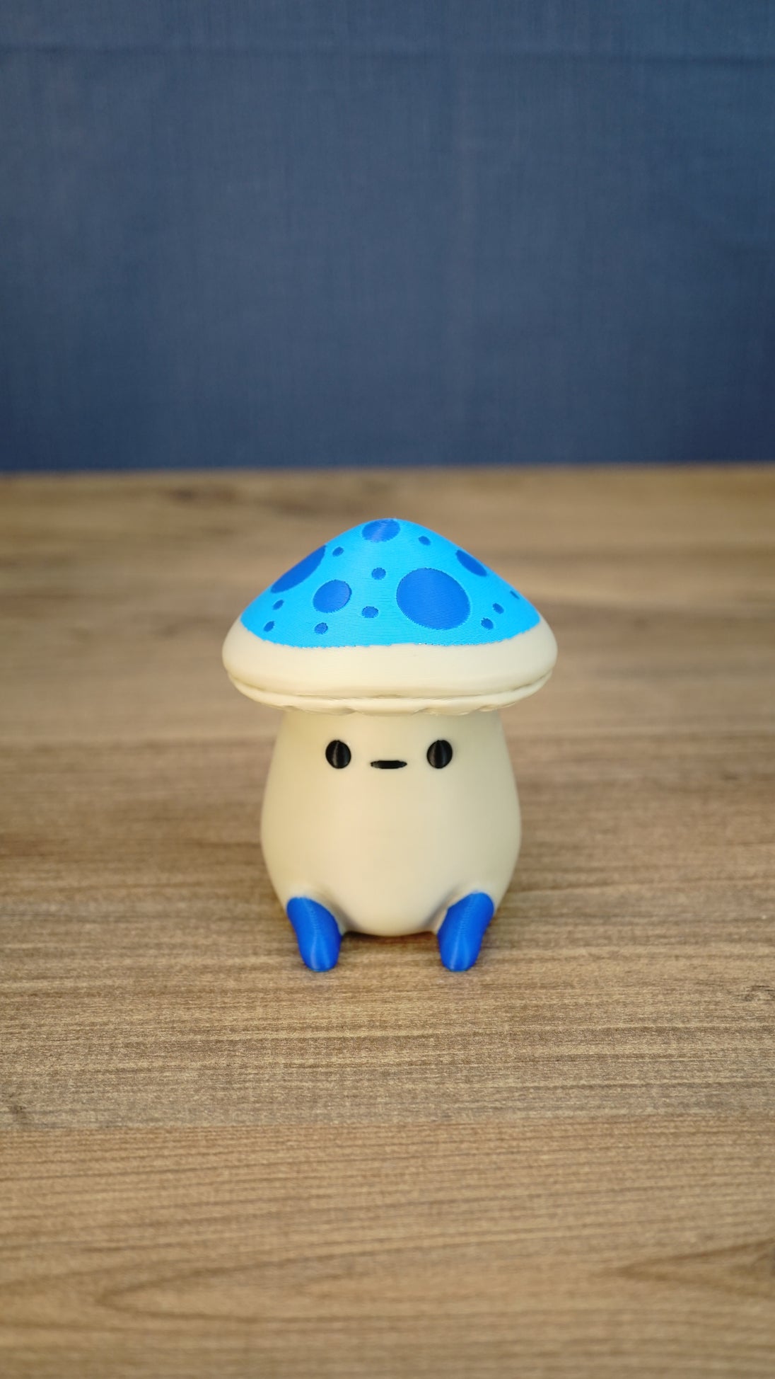 Front view of an Elderwood Fun Guy figurine with a blue spotted mushroom cap, cream body, black eyes, and blue feet.