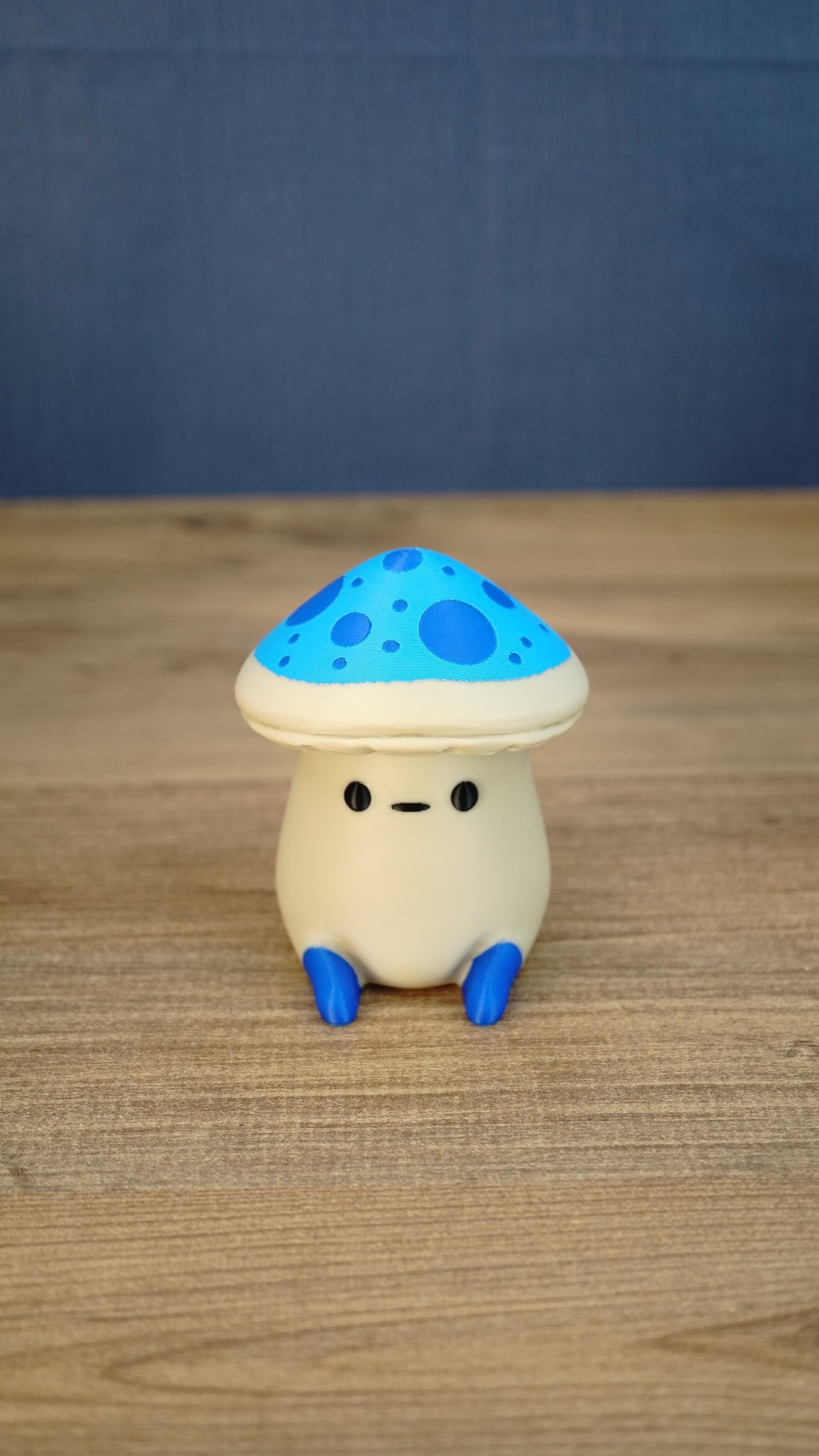 Front view of an Elderwood Fun Guy figurine with a blue spotted mushroom cap, cream body, black eyes, and blue feet.