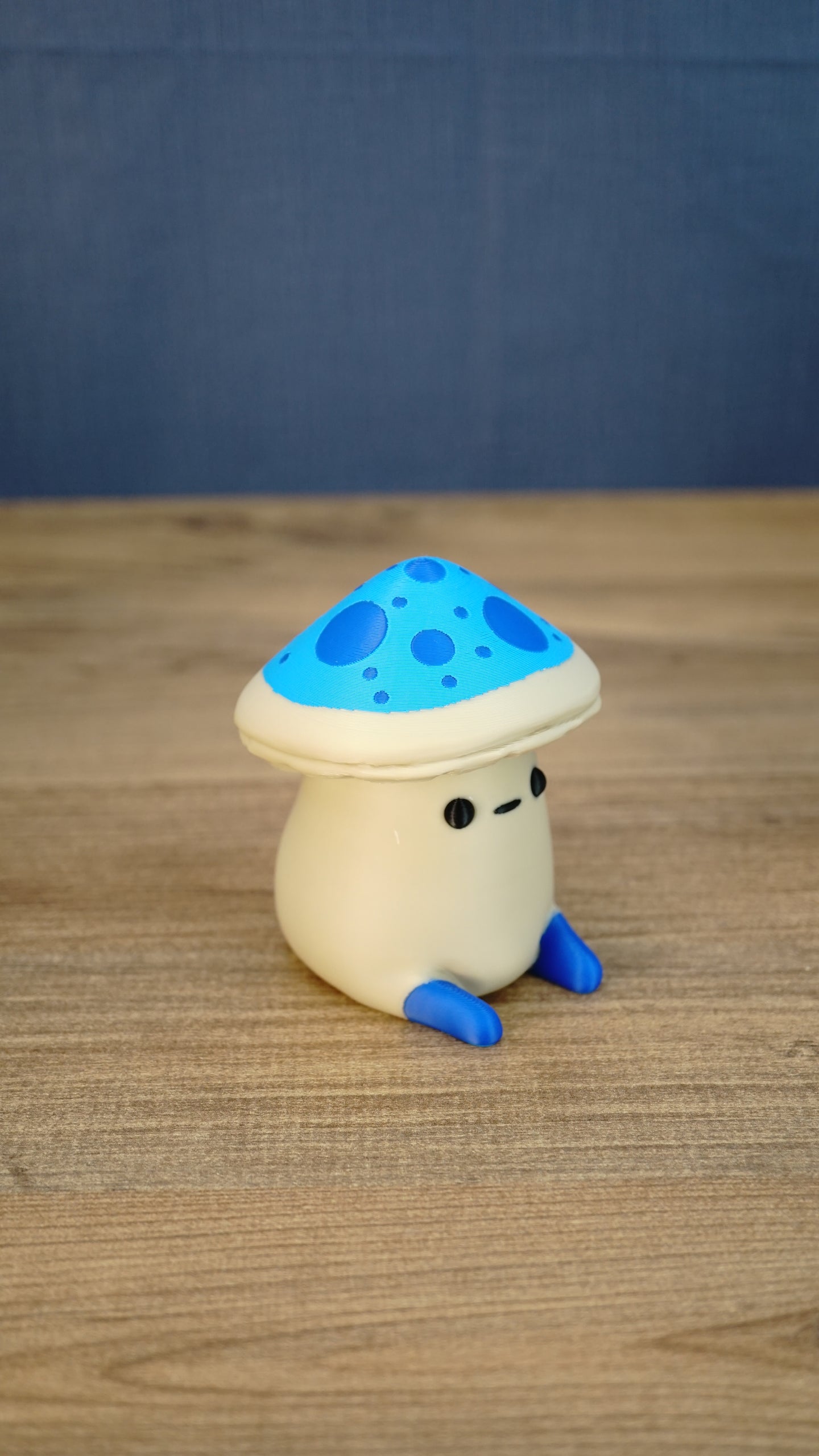 Side view of the Elderwood Fun Guy figurine showing its cream body, blue feet, and bright blue mushroom cap with darker blue spots.