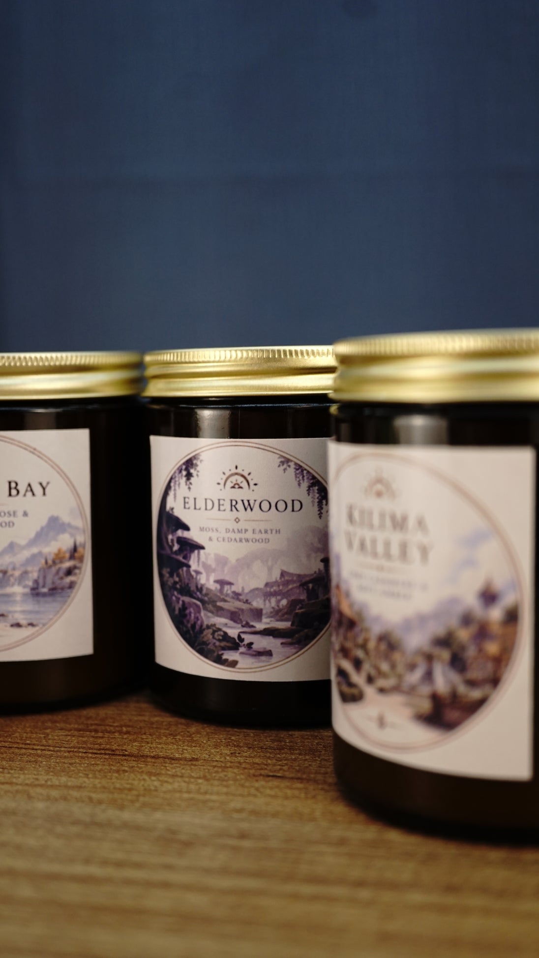 Elderwood soy wax candle in focus with moss, damp earth and cedarwood fragrance, framed by Bahari Bay and Kilima Valley candles.