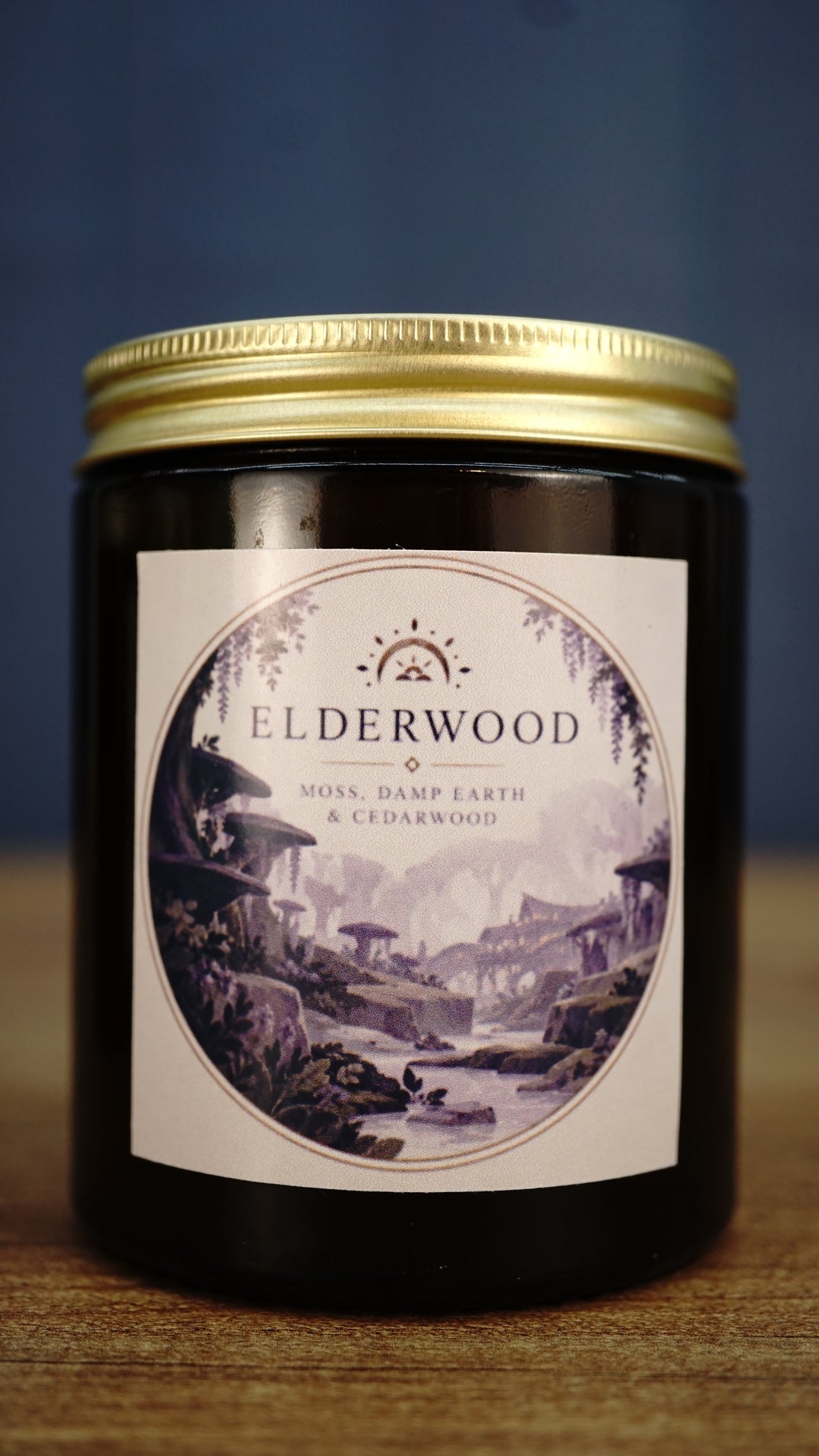 Elderwood vegan soy wax candle in an amber glass jar with gold lid, featuring moss, damp earth and cedarwood woodland fragrance.