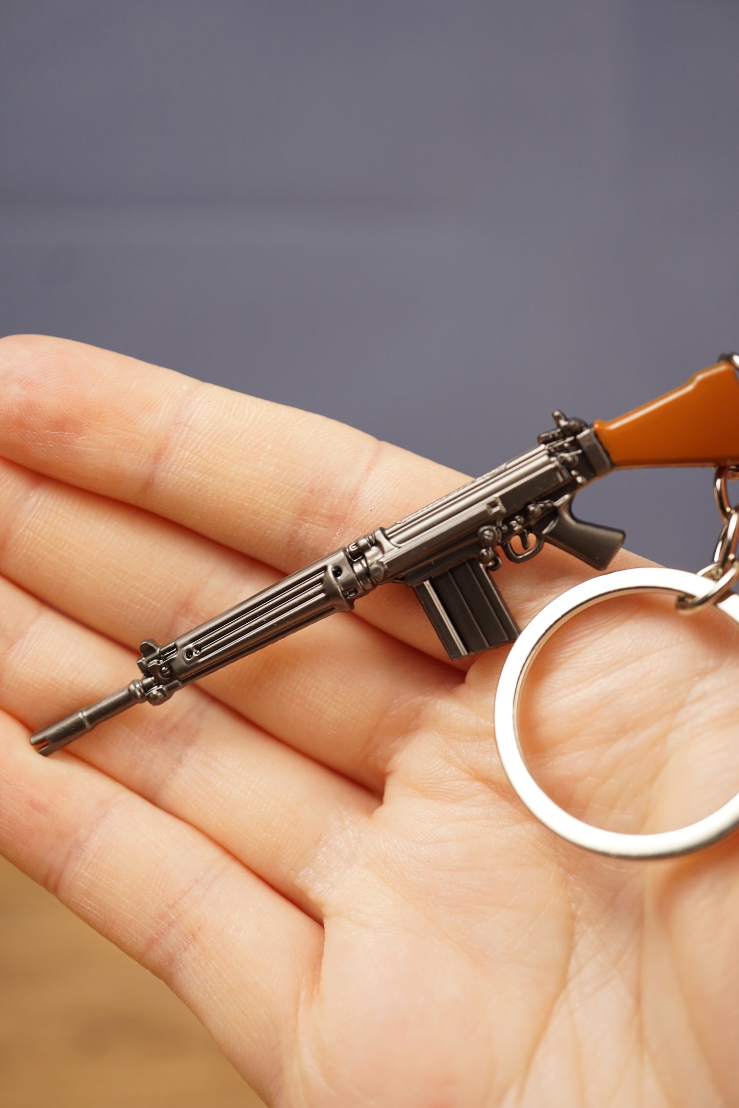 Detailed base FAL rifle keychain resting across a hand, with gunmetal body, brown stock and silver keyring visible