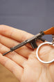 Detailed base FAL rifle keychain resting across a hand, with gunmetal body, brown stock and silver keyring visible