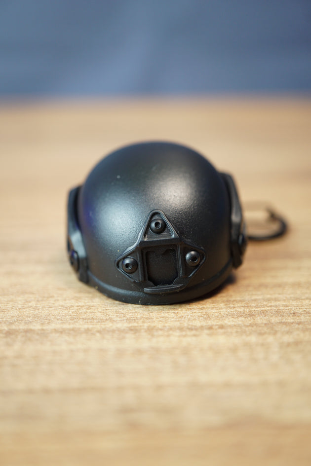 Front view of a black FAST MT helmet bottle opener keychain with tactical mount details, rounded helmet shell, and compact desk display.
